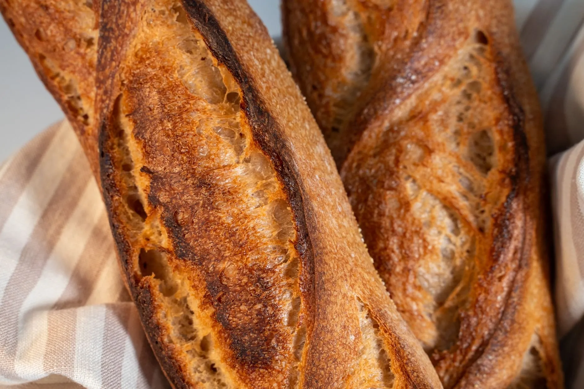 Two dark-baked baguettes with open scores resting on a striped linen cloth