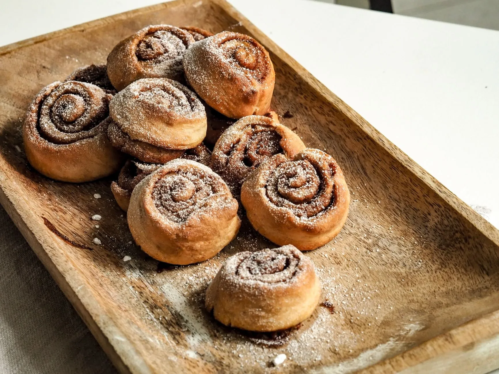 A wooden tray of cinnamon buns dusted with sugar