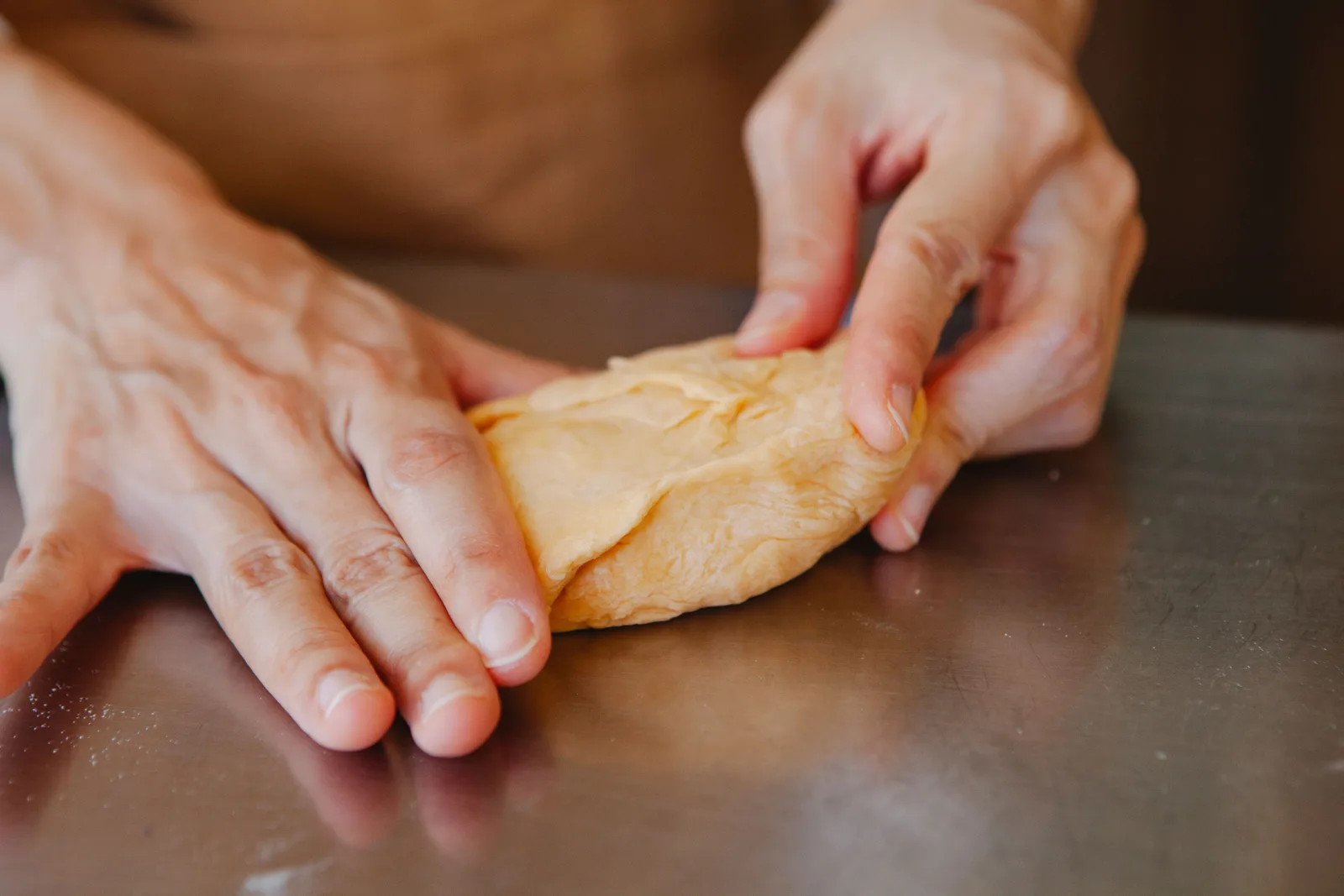 A baker dusts flour over dough on a dark bench